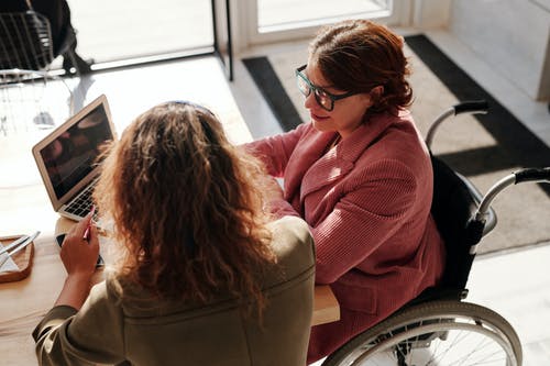 woman in wheelchair talking to woman sitting in front of computer