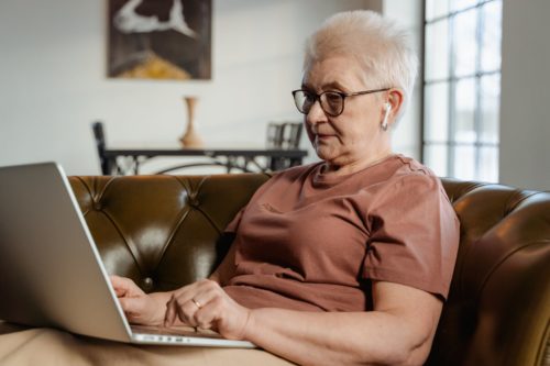 elderly woman sitting on couch and using laptop