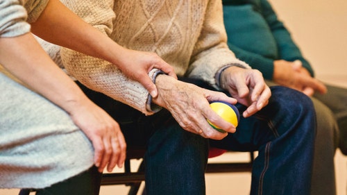 person sitting next to and holding the arm of elderly person